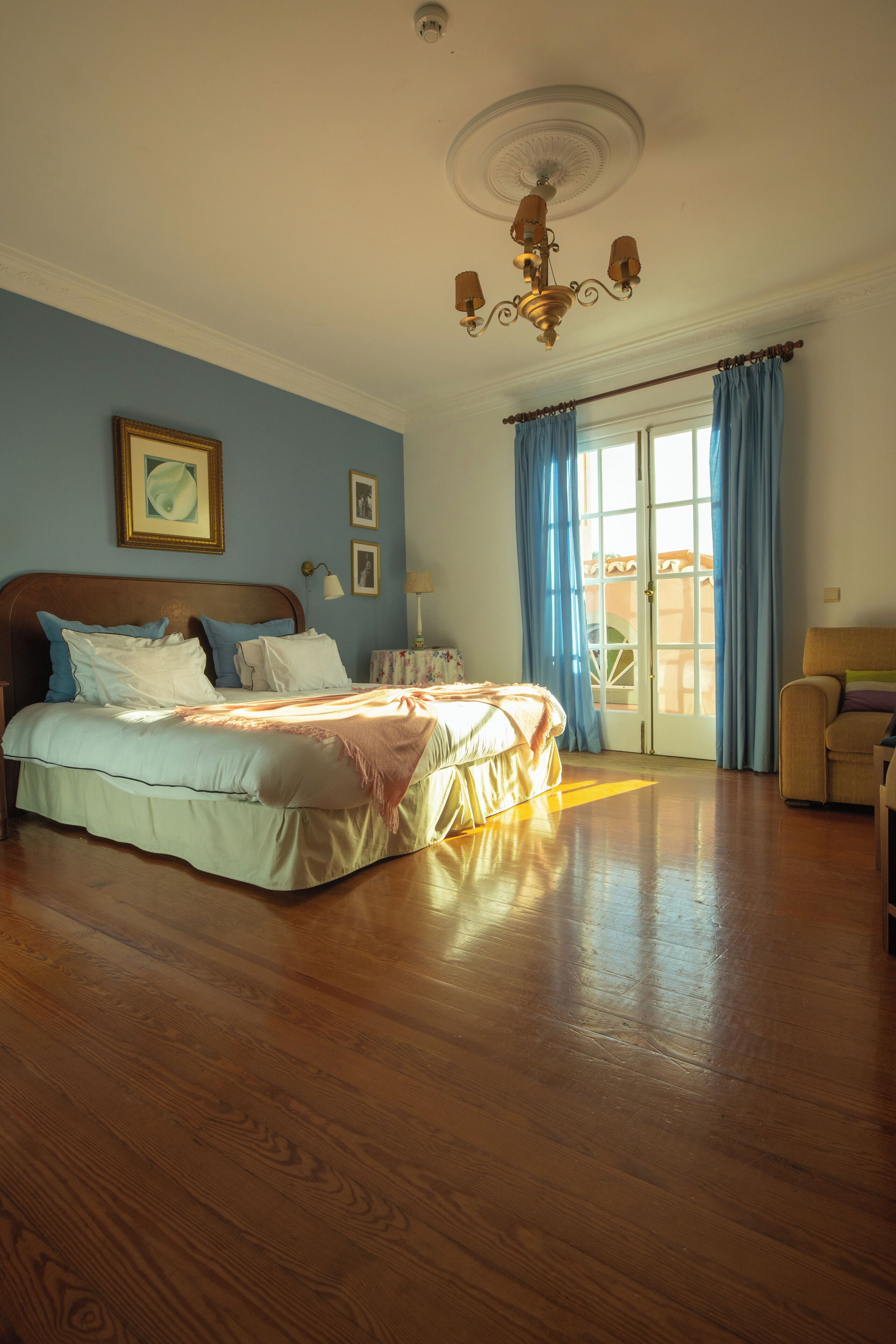 A bedroom with a large bed, a chandelier, and a view of the outside through a door with curtains.