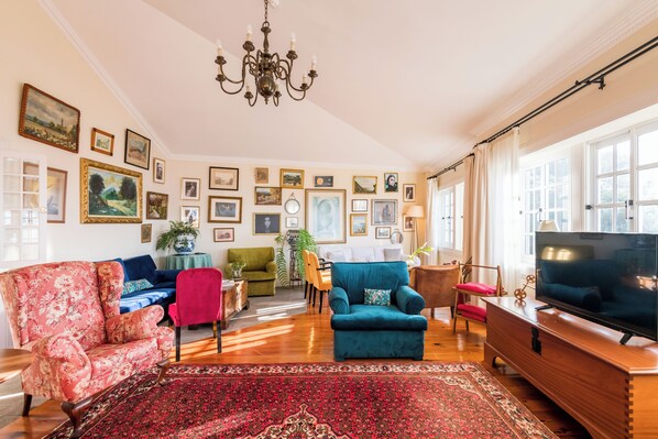 A living room with a large TV, multiple sofas, a red carpet, and framed pictures on the wall. - Villa Alto Boutique Hotel (Ponta do Sol)