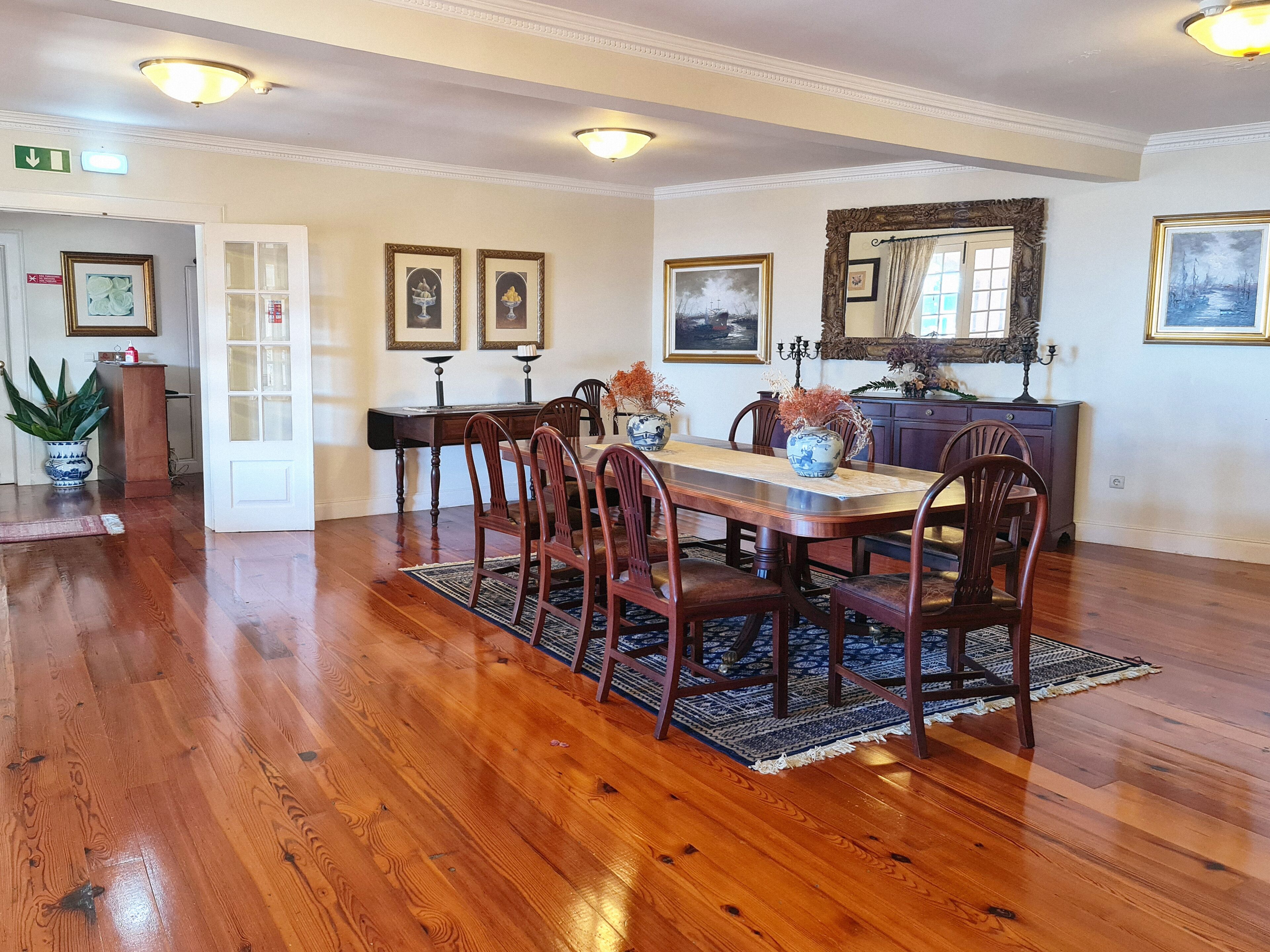 A dining room with a wooden table, chairs, and a rug. There are framed pictures on the walls and a mirror above the table.