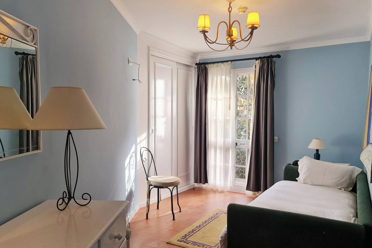 Un dormitorio con cama, una silla, cómoda, lámpara y candelabro.