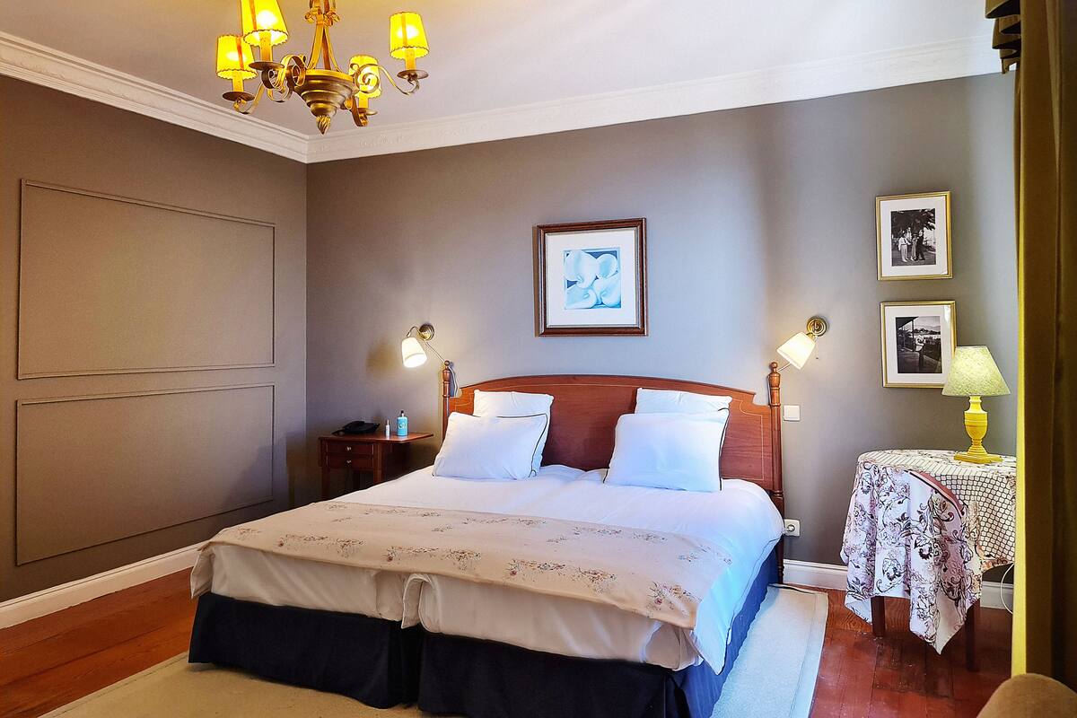 Een keurig opgemaakt slaapkamer met een groot bed, nachtkastjes, een kroonluchter en lijstjes met foto's aan de muur.