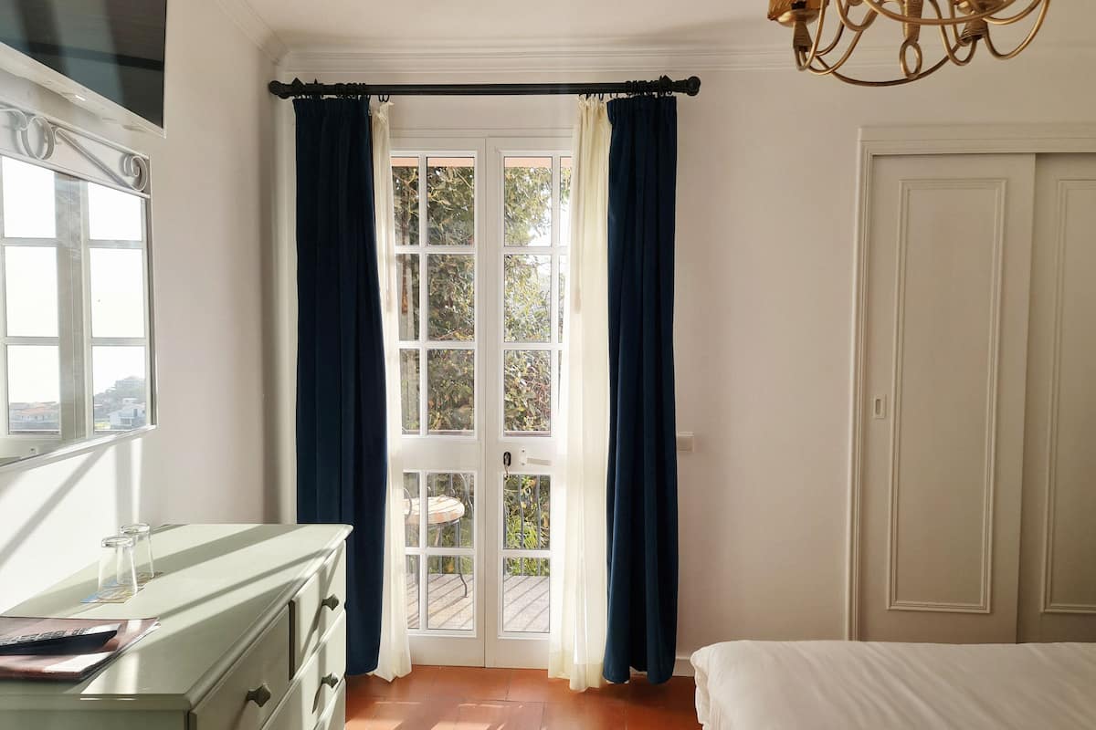 Een slaapkamer met een bed, een dressoir, een raam met gordijnen en een deur.