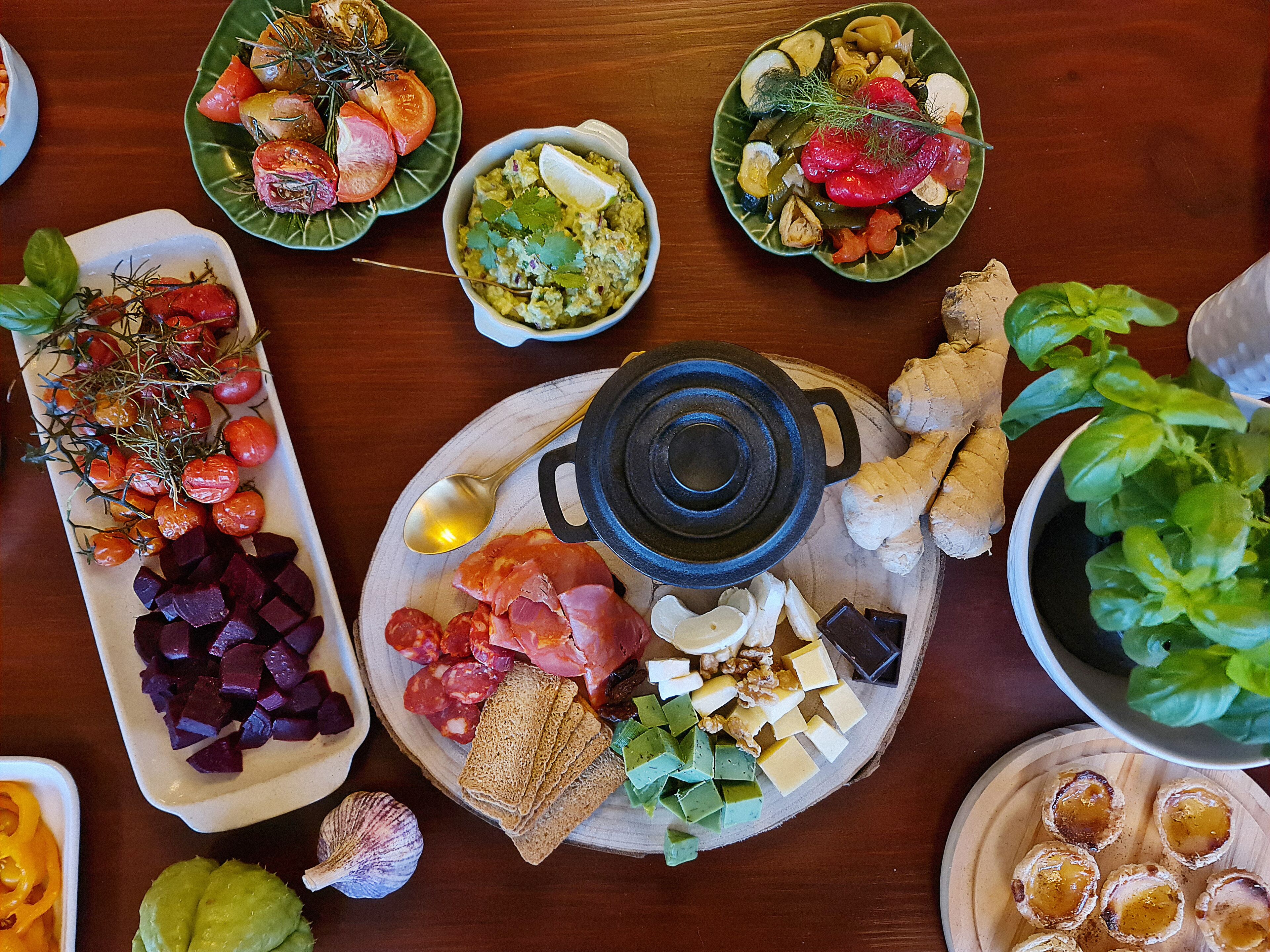 Une variété d’aliments sont disposés sur une table en bois, notamment des assiettes de légumes coupés, de viandes, de fromages et du pain.