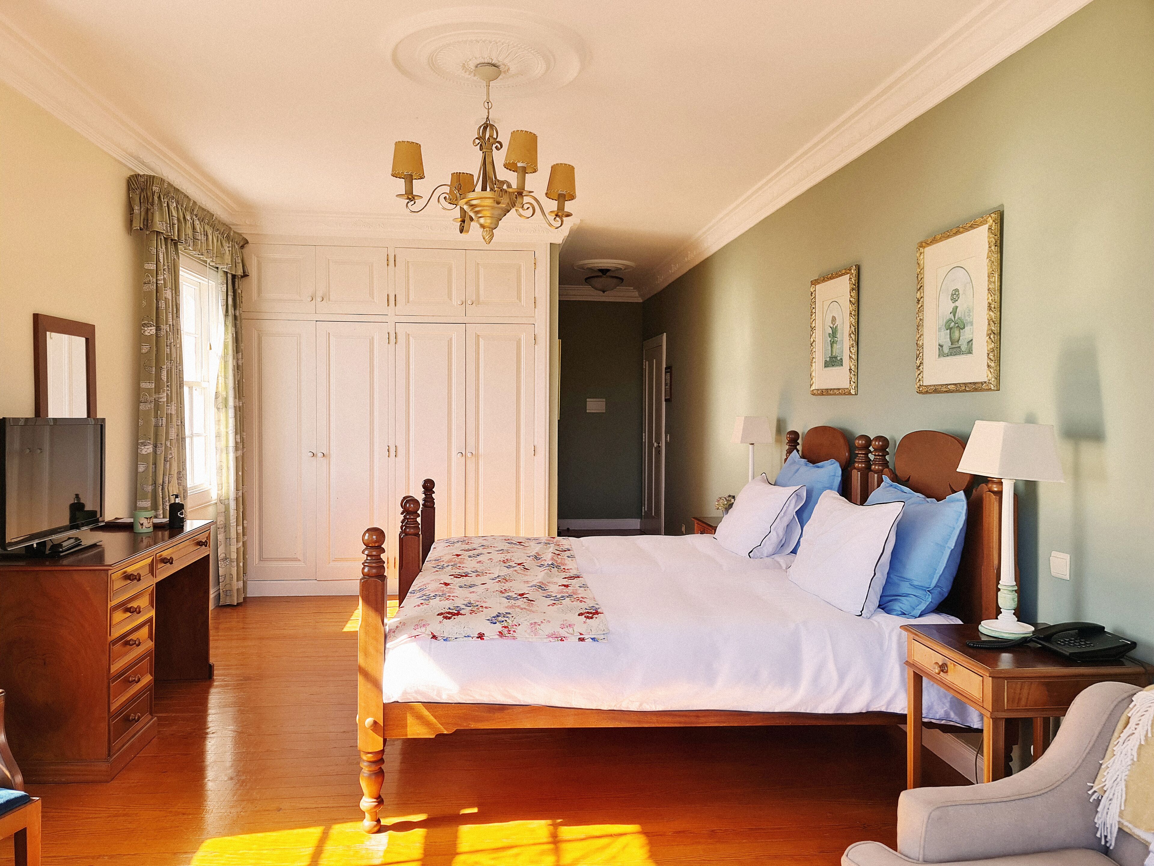 A neatly arranged bedroom with a wooden bed, a television on a dresser, and a chandelier.