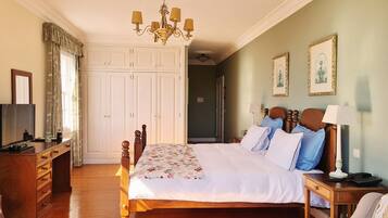 A neatly arranged bedroom with a wooden bed, a television on a dresser, and a chandelier.