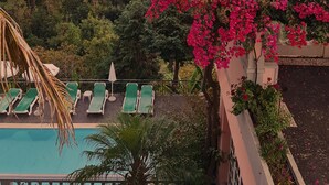 Zona de piscina con sillas reclinables verdes, una palmera y flores de buganvilla rosadas.