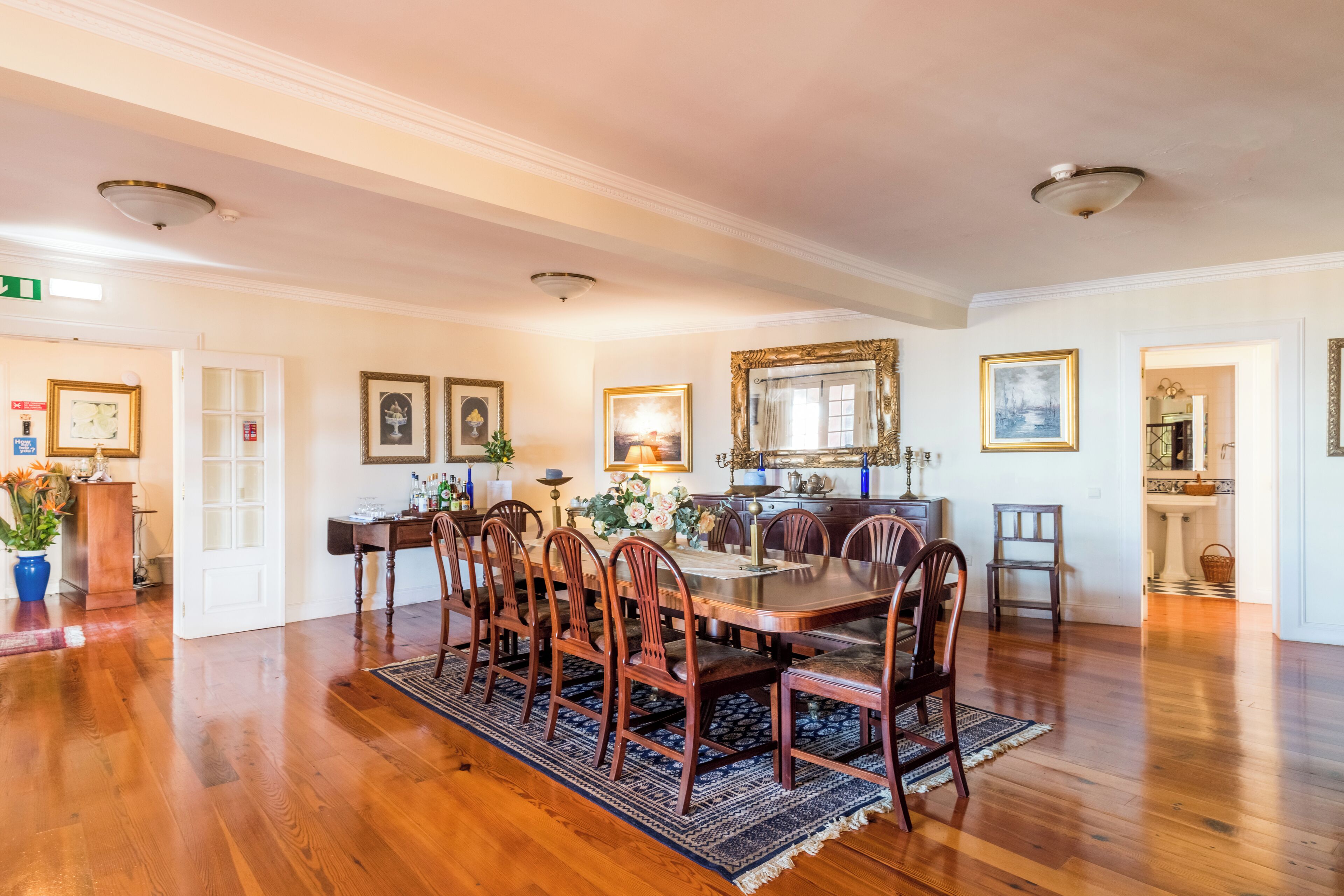A dining room with a wooden table and chairs, surrounded by framed artwork and a chandelier.