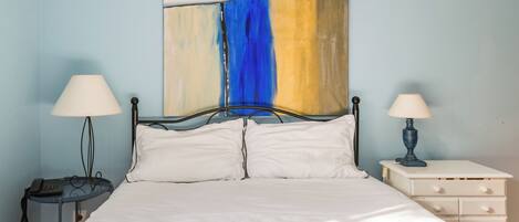 A bed with white linens, two bedside tables with lamps, a wall art piece, and a nightstand with drawers.