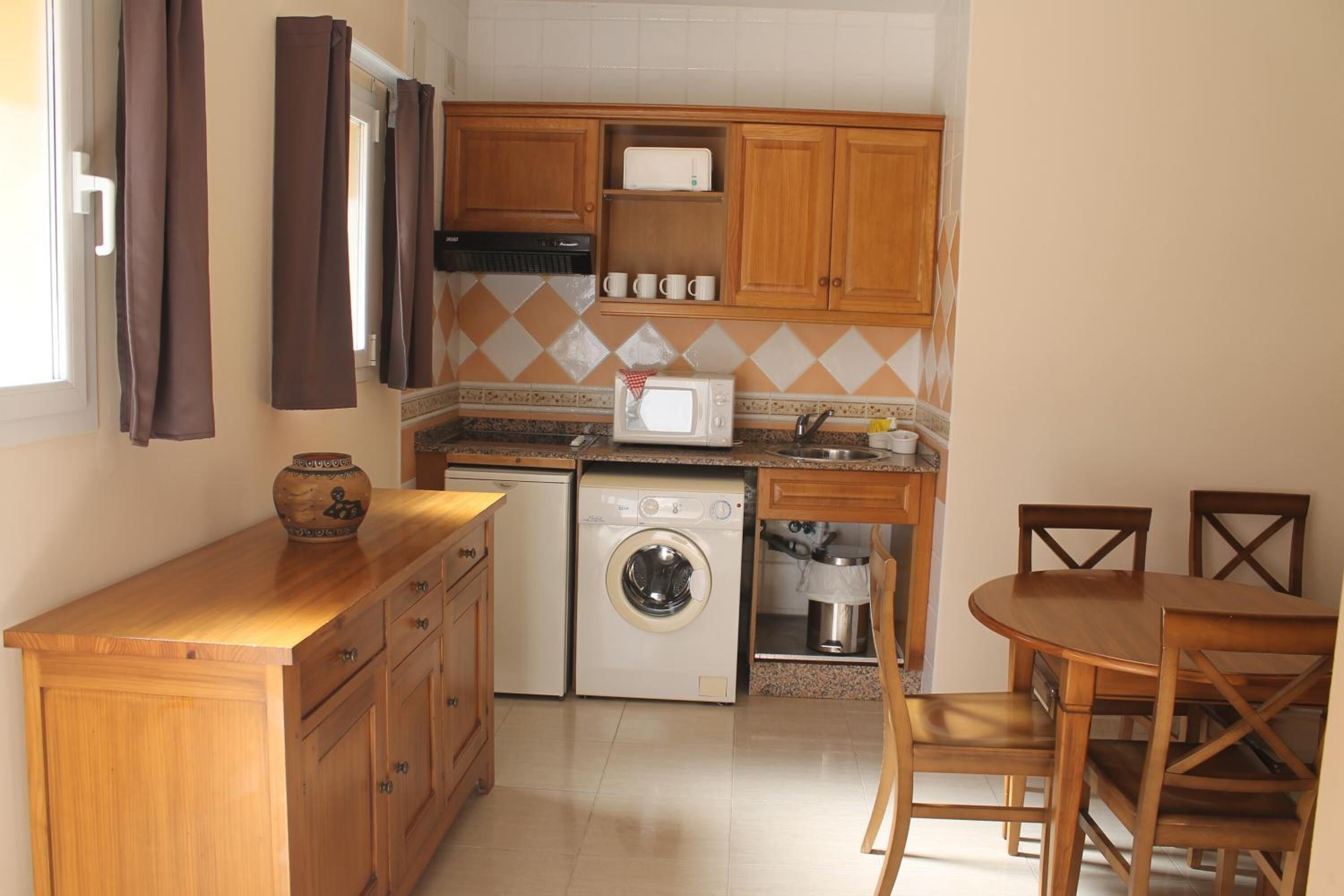 Una cucina compatta con mobili in legno, lavatrice, microonde e zona pranzo con tavolo e sedie.