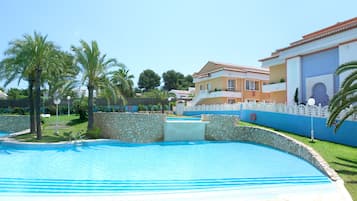 Una piscina con borde de piedra, palmeras y un edificio de fachada azul y blanca.