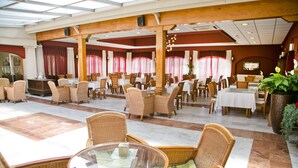 Un amplio comedor interior con varias mesas y sillas, vigas de madera y ventanas grandes con cortinas.