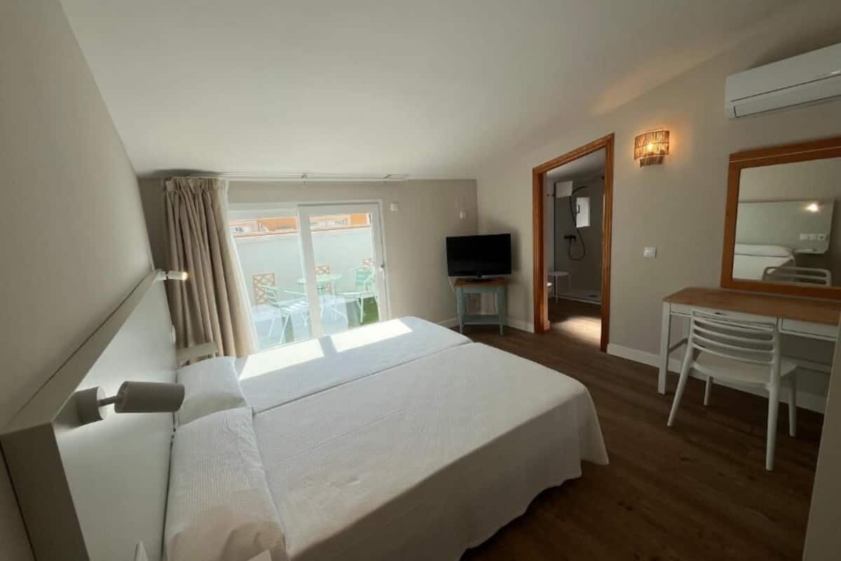 A hotel room with a bed, a desk, a chair, a television, and a balcony with a view.