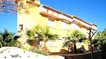 Un bâtiment jaune, doté de nombreuses fenêtres et d’un toit incurvé, entouré de palmiers.
