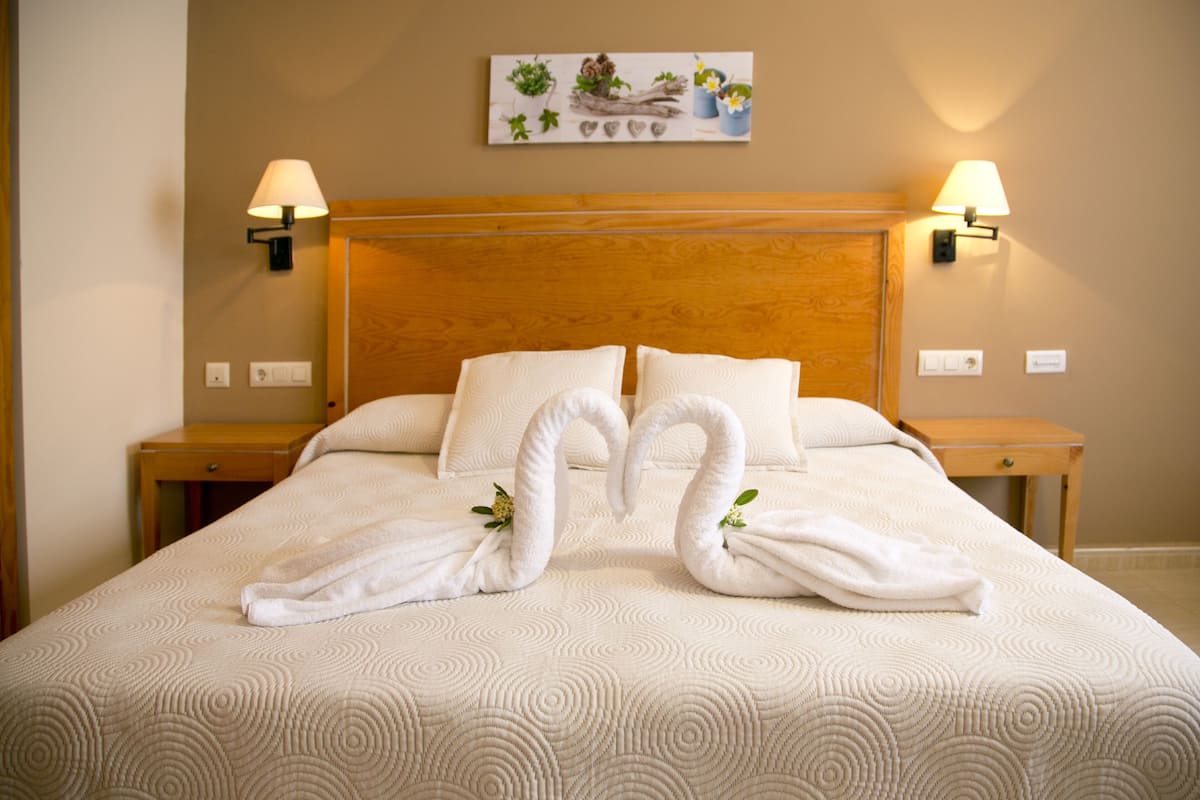 A hotel room with a large bed, two wall-mounted lamps, and a painting on the wall.