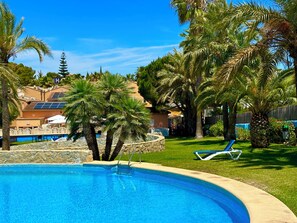 A swimming pool with a stone border, palm trees, and a clear blue sky. - Aparthotel Pinosol (Javea)