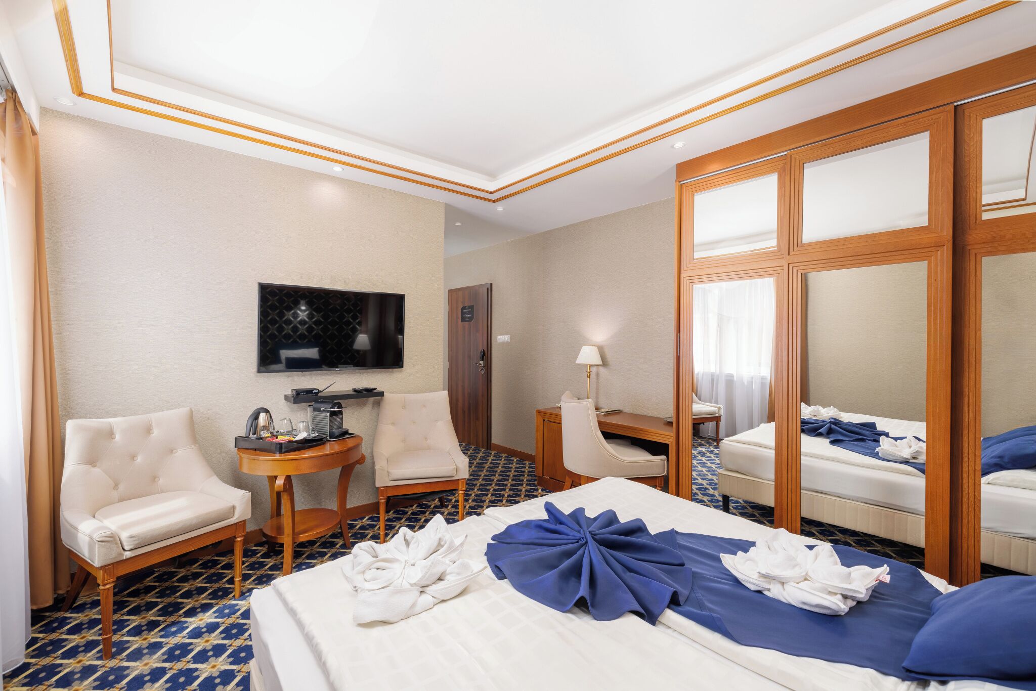 Una habitación de hotel con una cama grande, dos sillones, un escritorio, un televisor y un espejo.