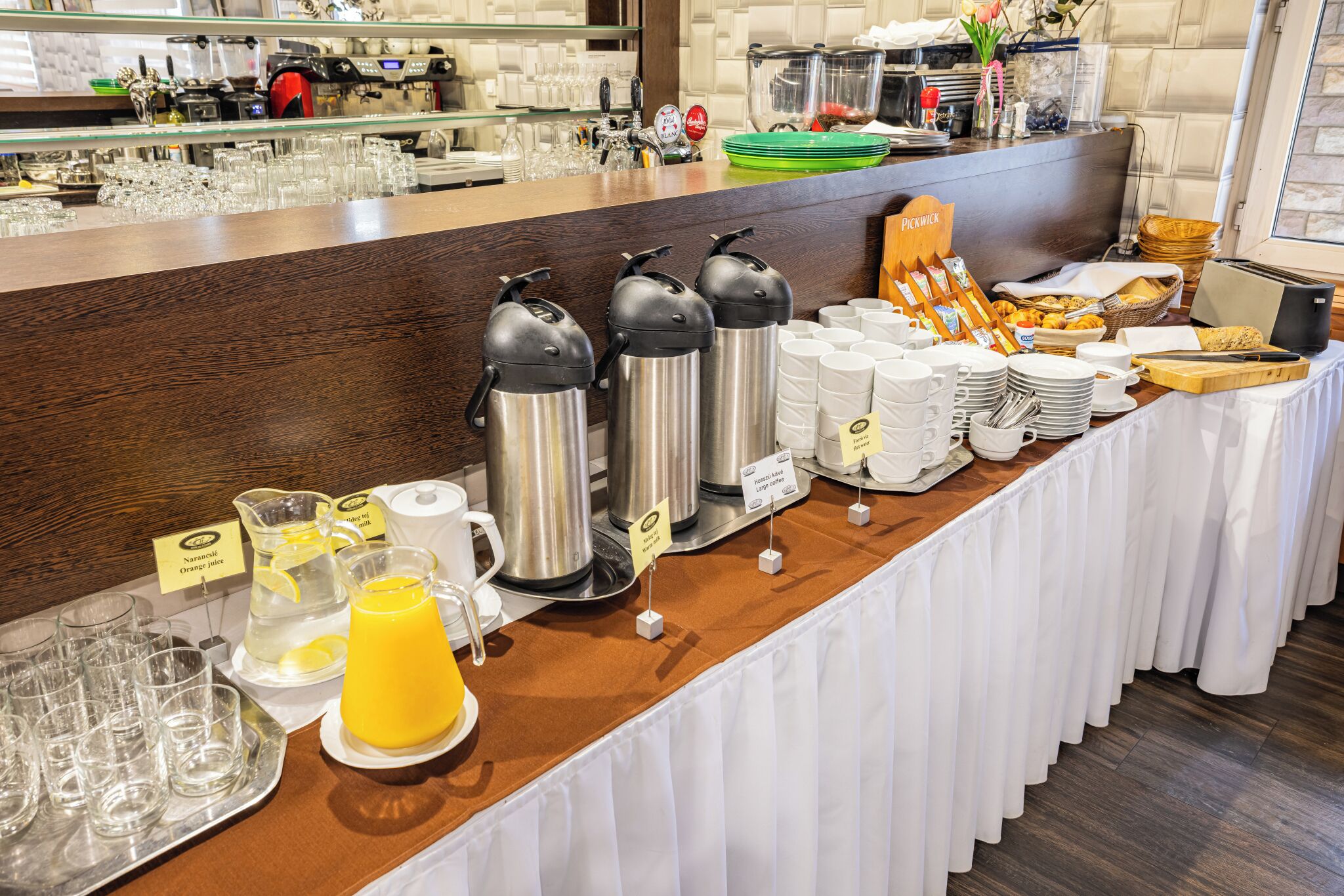 Una mesa de buffet con diversos alimentos, máquinas de café y dispensador de zumo.