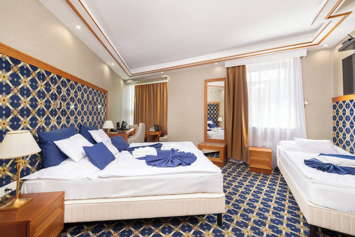 Een hotelkamer met een groot bed, een kleiner bed, een bureau, een stoel, een spiegel en een badkamergedeelte.