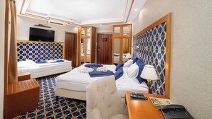 Habitación de hotel con cama, escritorio con teléfono, silla, televisor y puerta del baño.