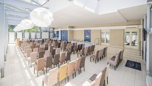 Una amplia sala de conferencias con filas de sillas, una mesa larga y un alto techo con tragaluces.