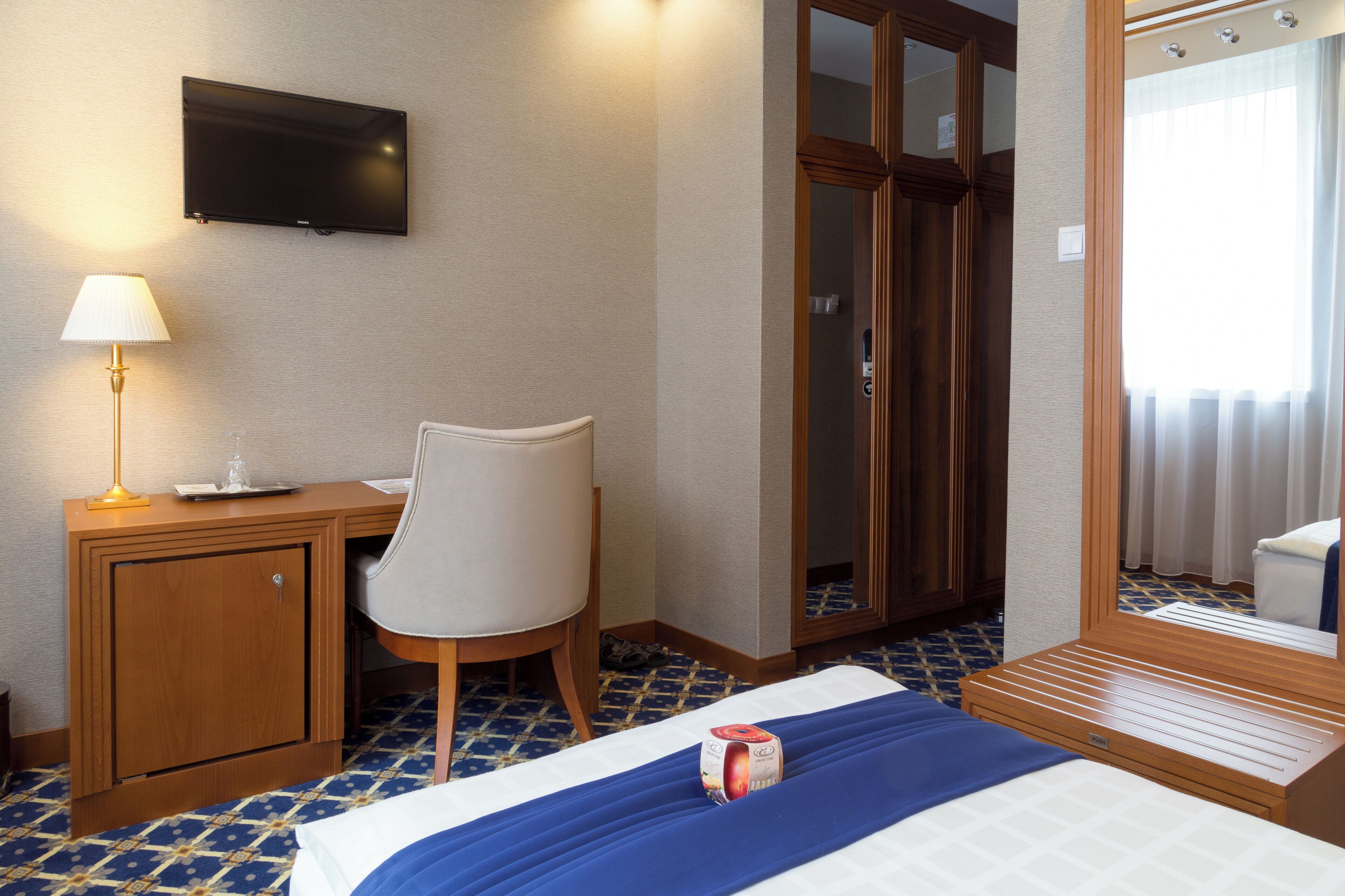 Una habitación de hotel con cama, escritorio, silla, televisión y armario.