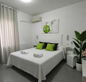 A hotel room with a neatly made bed, a potted plant, and a wall-mounted air conditioner. - Birillo (La Spezia)