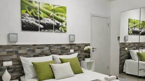 Quarto de hotel moderno com cama bem arrumada, mesa de cabeceira com abajur e um espelho grande.