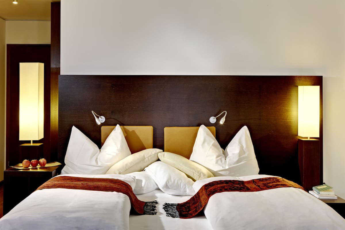 Une chambre d’hôtel avec un grand lit, deux lampes de chevet et une table de chevet sur laquelle se trouvent des pommes.