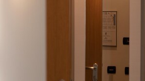 Entrada de una habitación de hotel con puerta de madera, lámpara de pared y timbre.