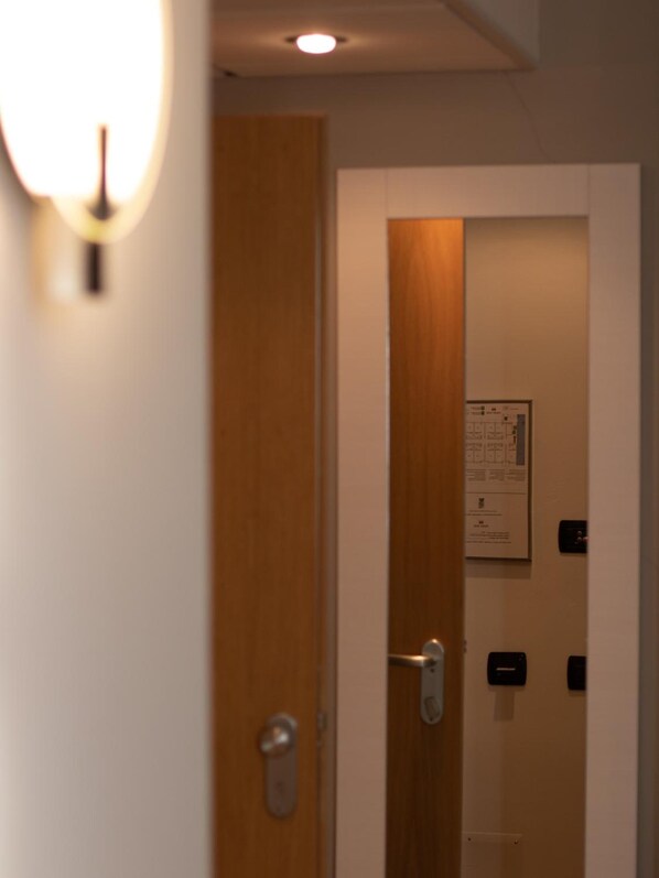 Entrada de una habitación de hotel con puerta de madera, lámpara de pared y timbre.