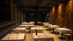Un restaurante con varias mesas y sillas, cada conjunto con cubiertos y copas de vino.