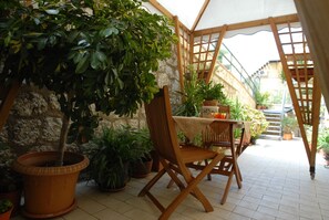 A covered patio with a wooden table and chairs, surrounded by potted plants and a stone wall. - Il Mandorlo (Agrigento)