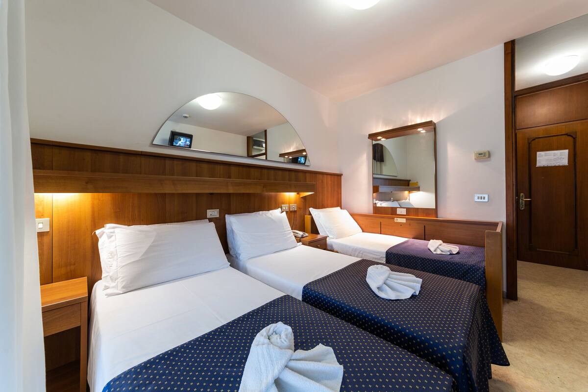 A hotel room with two beds, wooden headboards, a large mirror, and a wooden door.