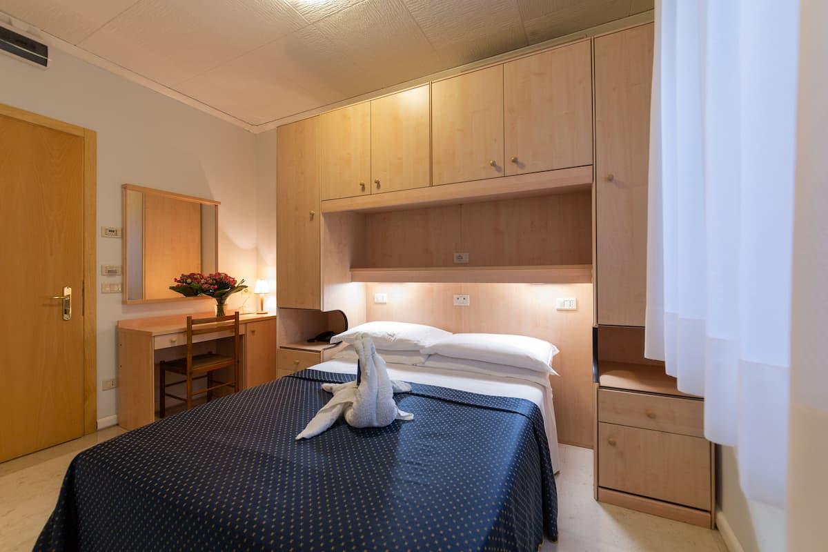A hotel room with a bed, wooden wardrobe, desk, and chair.