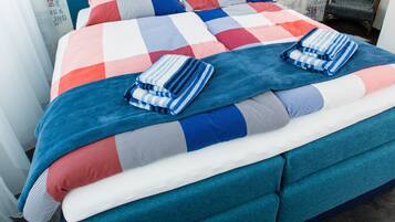 A neatly made bed with a checkered bedspread and blue and white striped pillows, set against a wall with a repeating pattern of 'Surfing & Sailing' text.