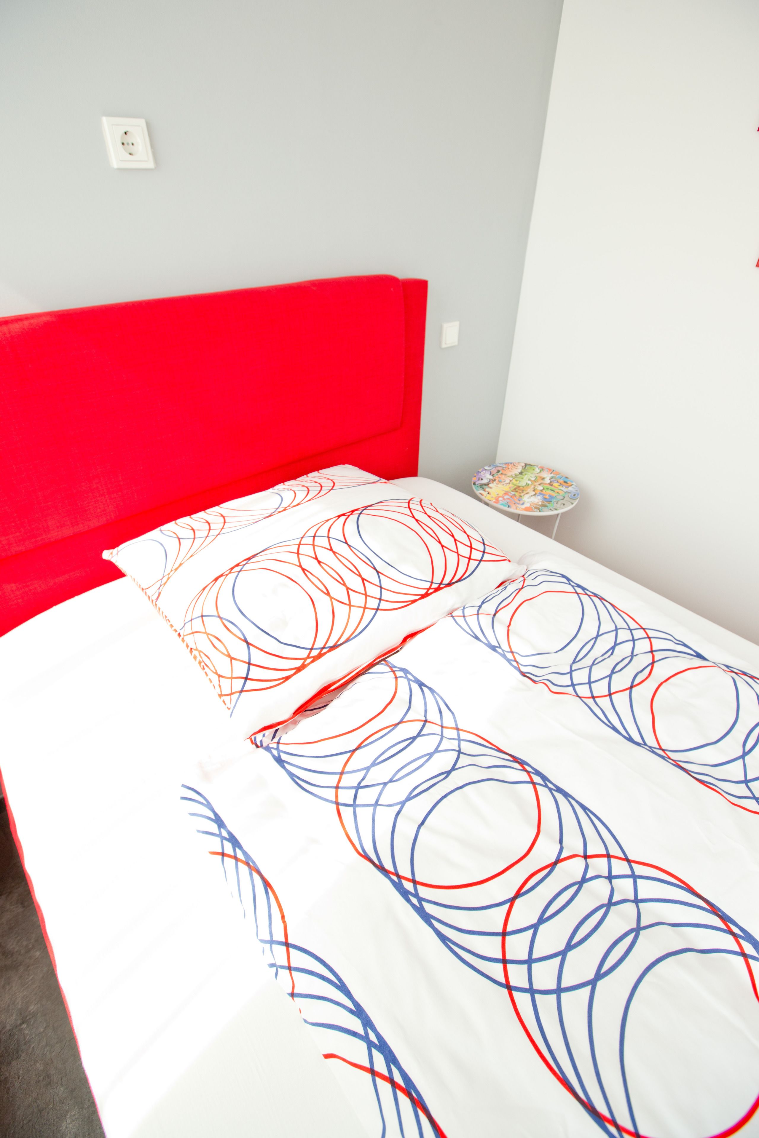 A bed with a red headboard and white bedding with red and blue patterns.