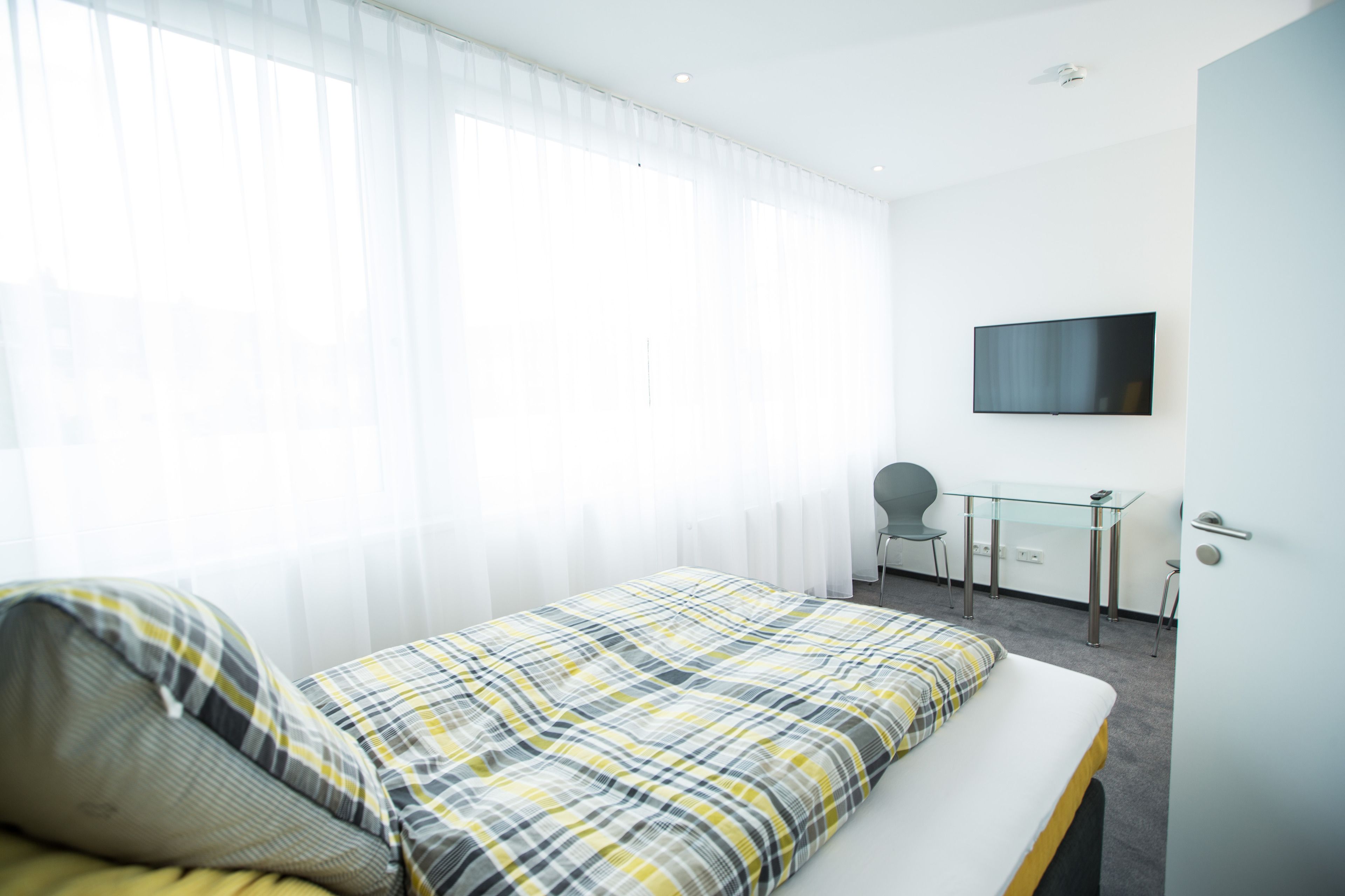 Une chambre d’hôtel avec un lit, un bureau, une chaise et un téléviseur fixé au mur.