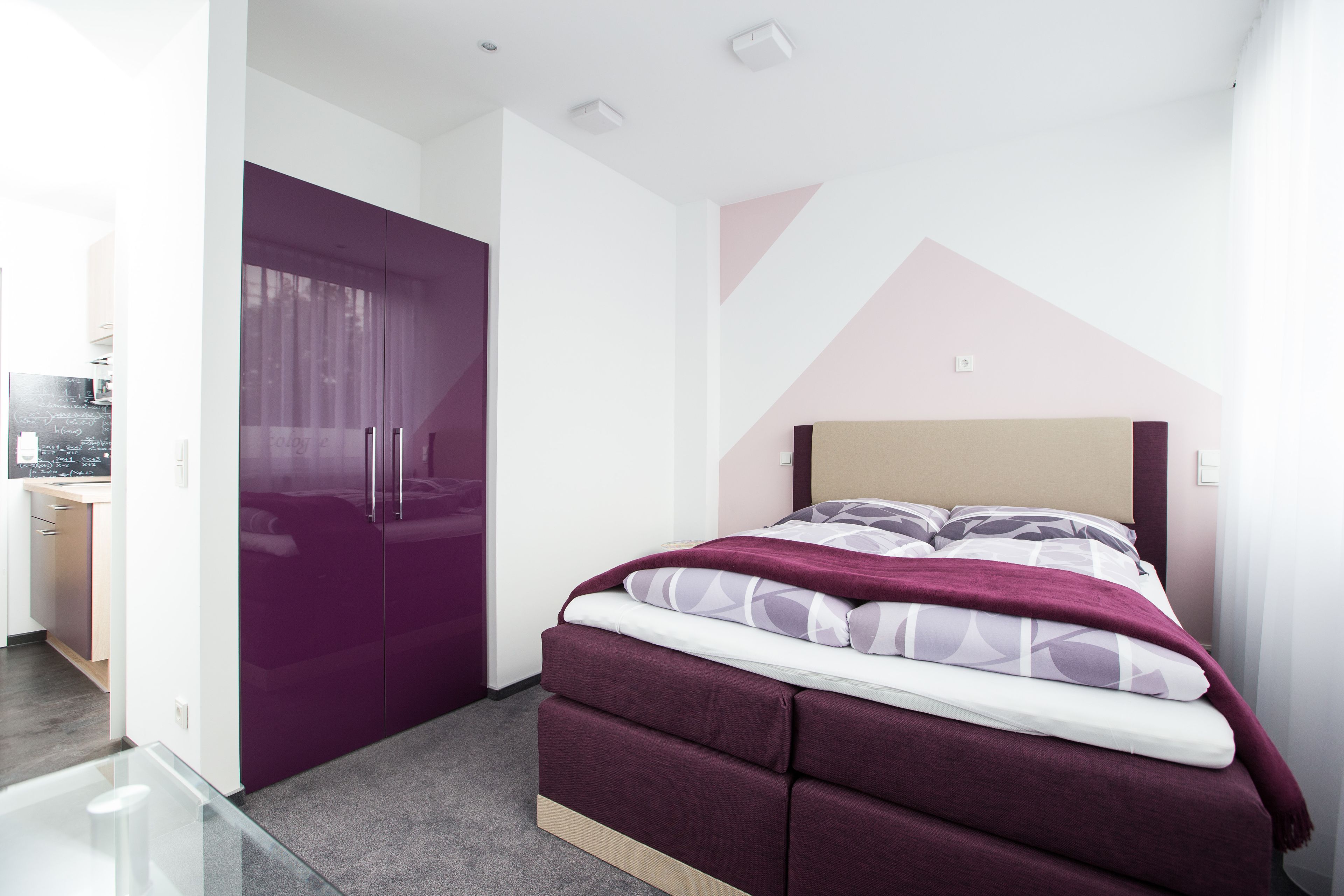 A modern bedroom with a bed, a purple wardrobe, and a desk area.