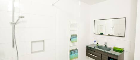 A modern bathroom with a glass shower enclosure, a vanity with a mirror, and a towel rack.