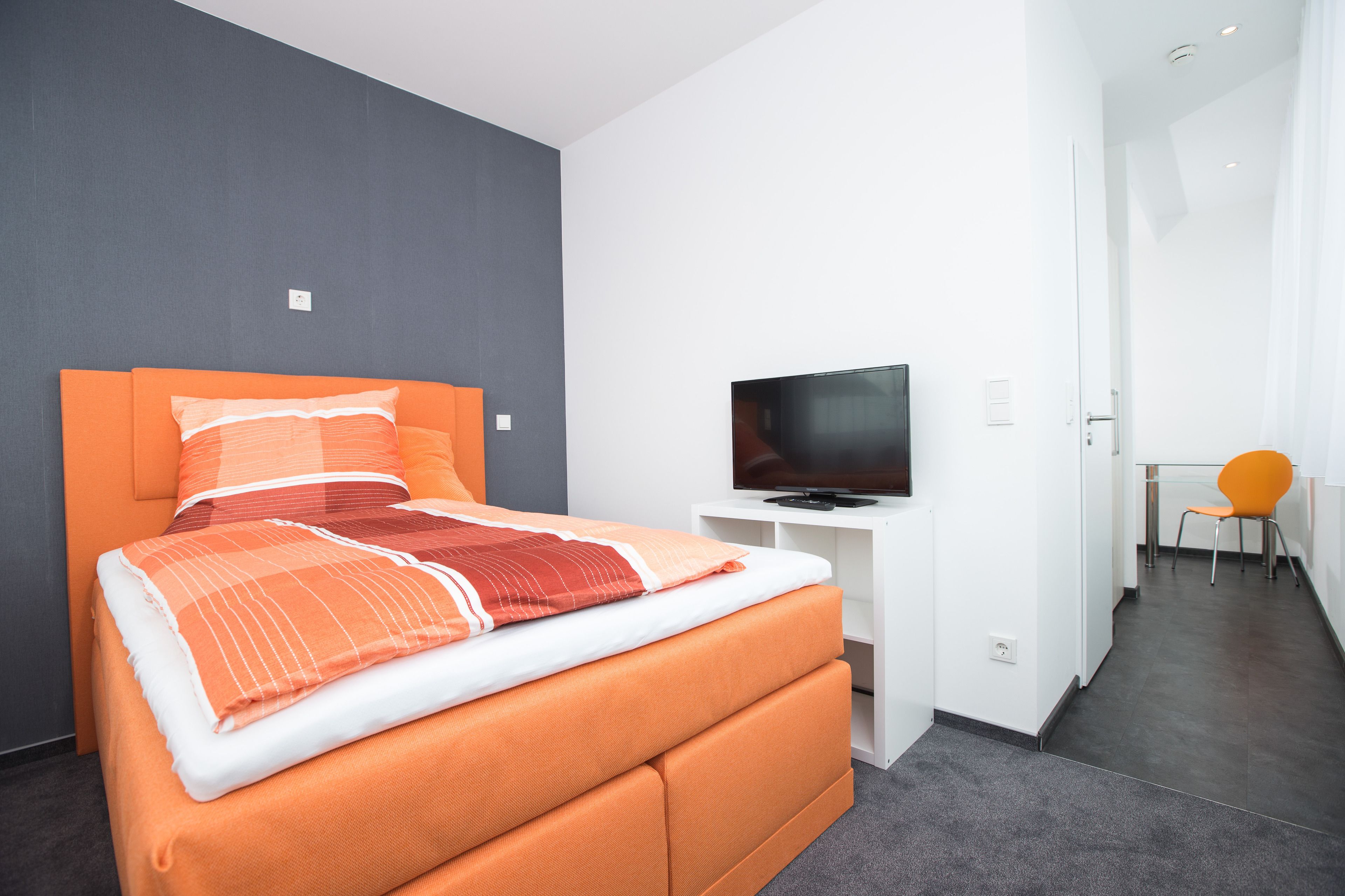 Une chambre d’hôtel moderne avec un grand lit, un téléviseur à écran plat et un fauteuil orange vif.