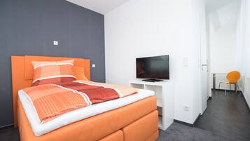 Une chambre d’hôtel moderne avec un grand lit, un téléviseur à écran plat et un fauteuil orange vif.