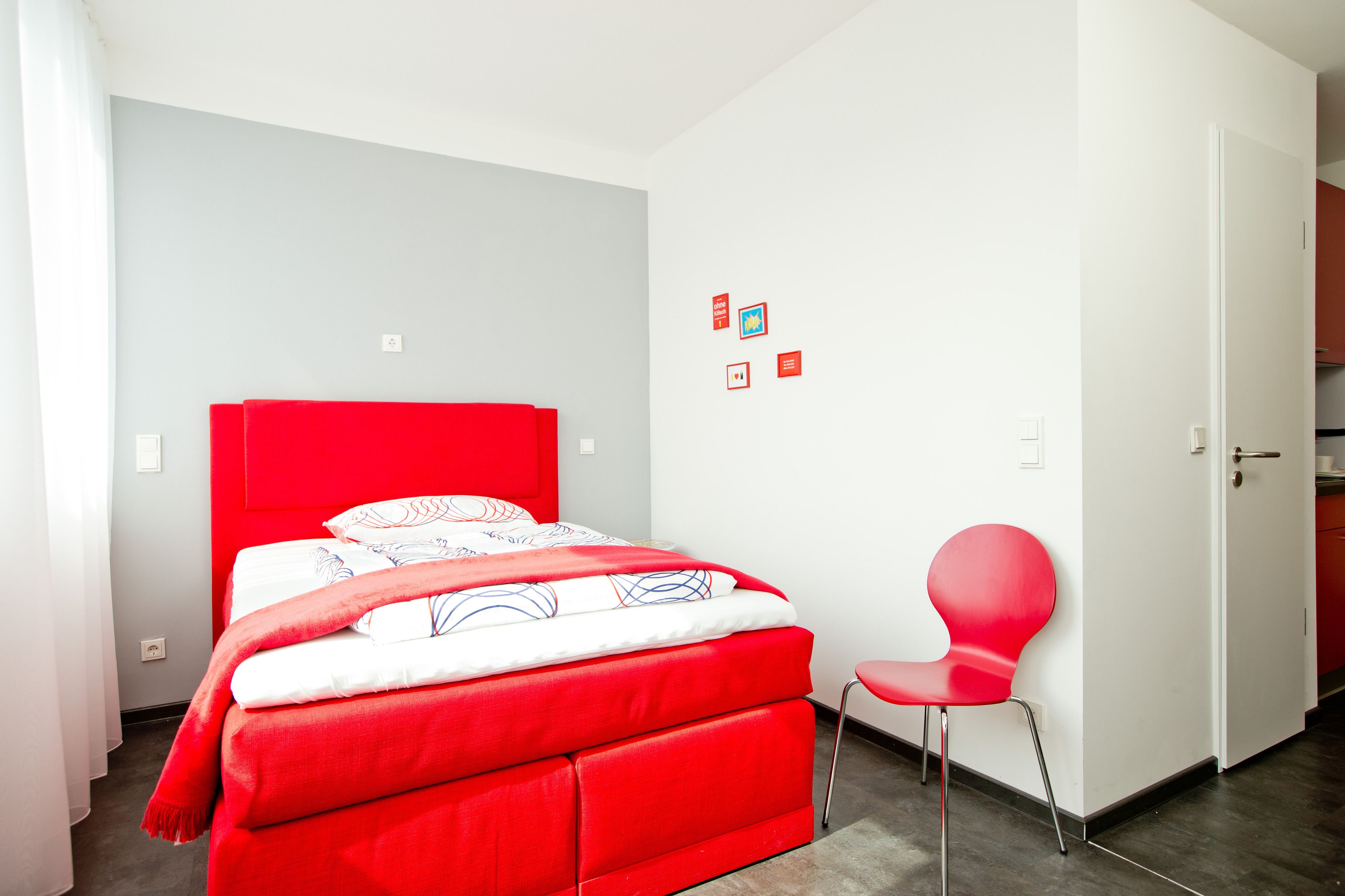 A modern bedroom with a red bed, white walls, and a red chair.