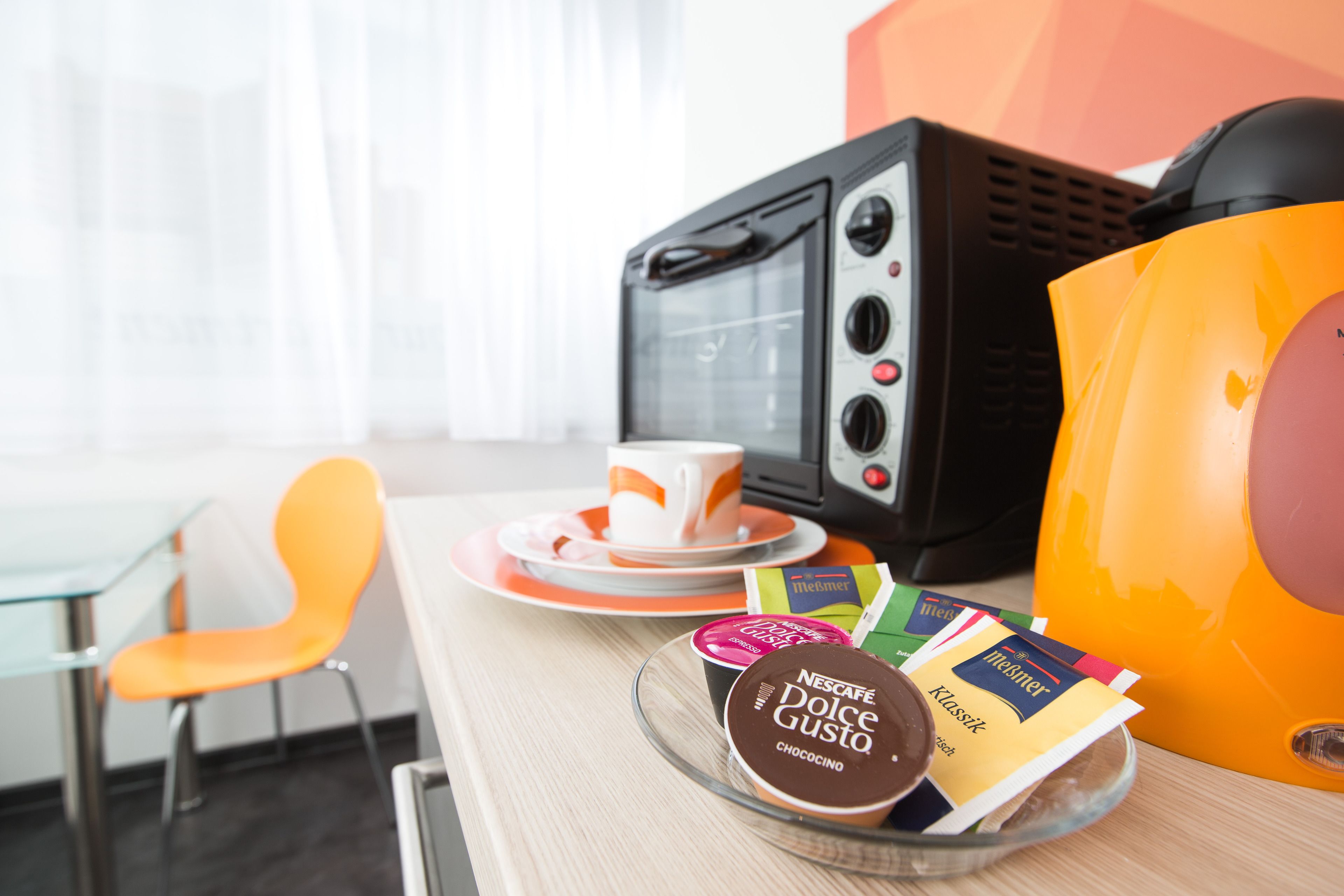 A breakfast setup with a coffee machine, a cup, and a plate with a coffee pod.