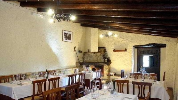 A restaurant with multiple tables set for dining, wooden beams on the ceiling, and a stone fireplace. - Tenuta Luogomarchese (Pollina)