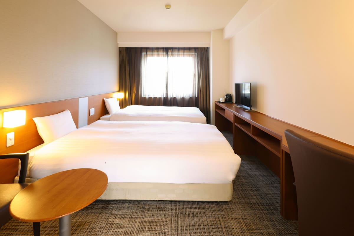 A hotel room with two beds, a desk, a chair, a television, and a window with curtains.