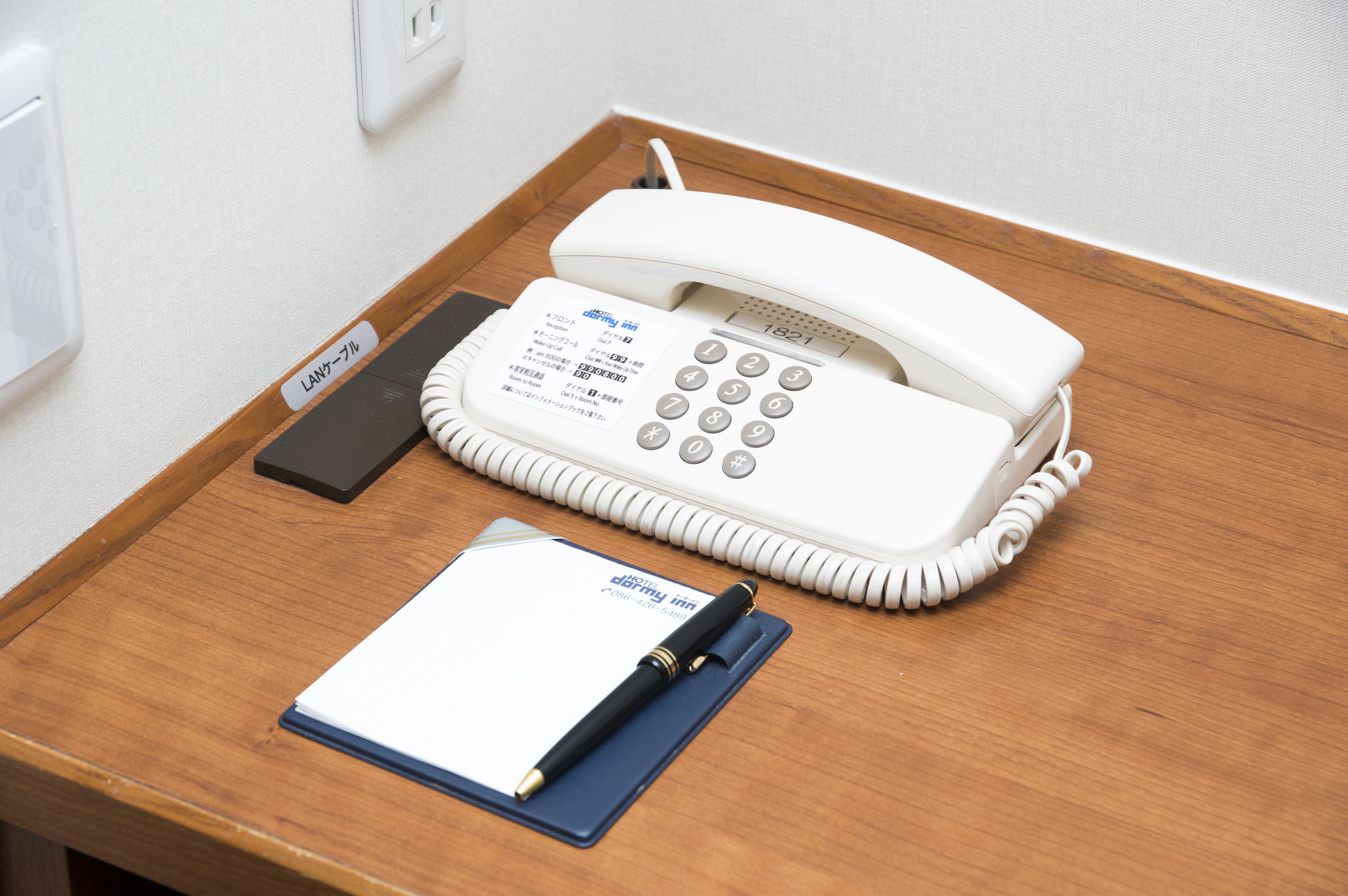 Un teléfono fijo blanco sobre un escritorio de madera, con un bloc de notas y un bolígrafo.