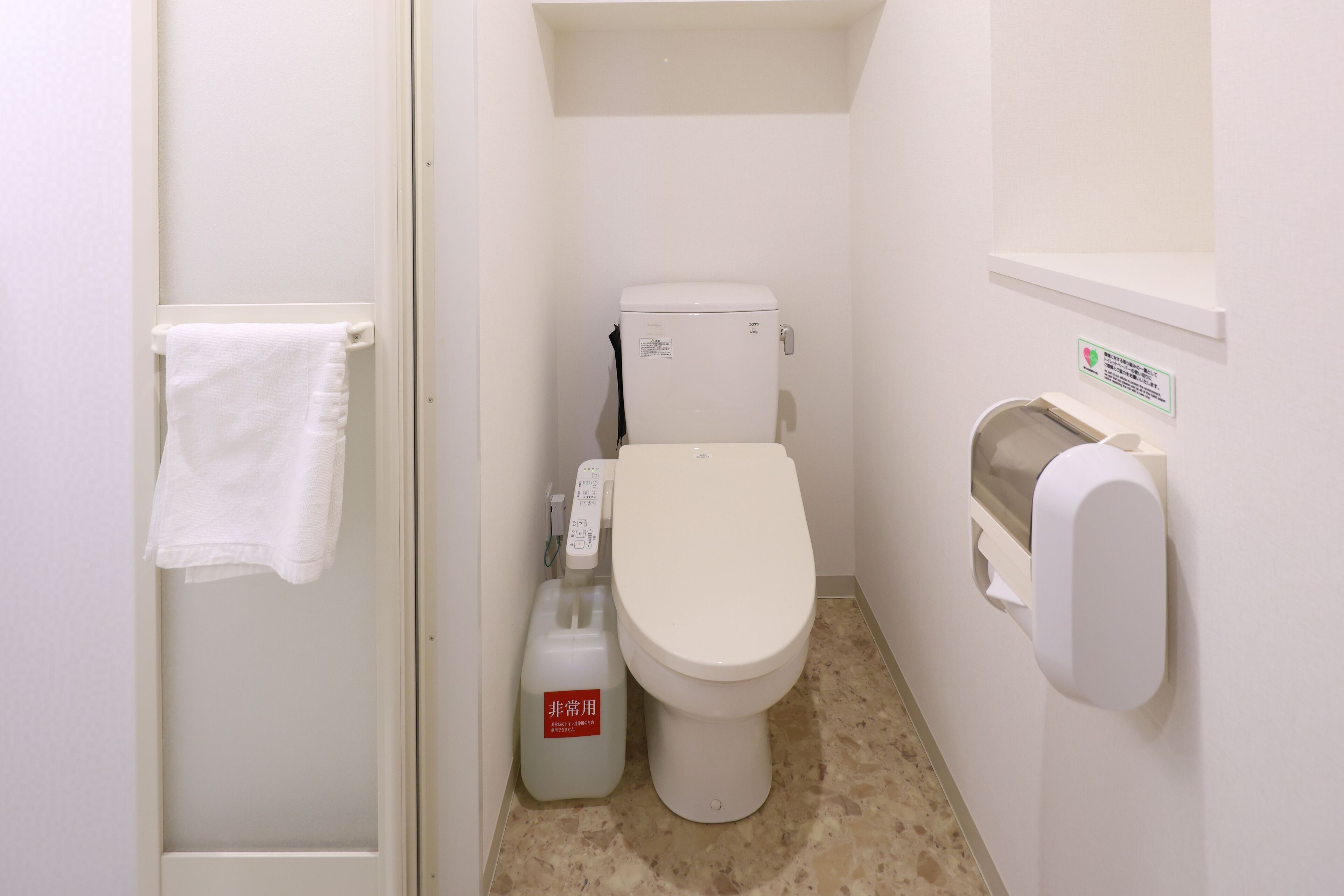 A small, clean bathroom with a toilet, a hand dryer, and a white towel hanging on a rack.