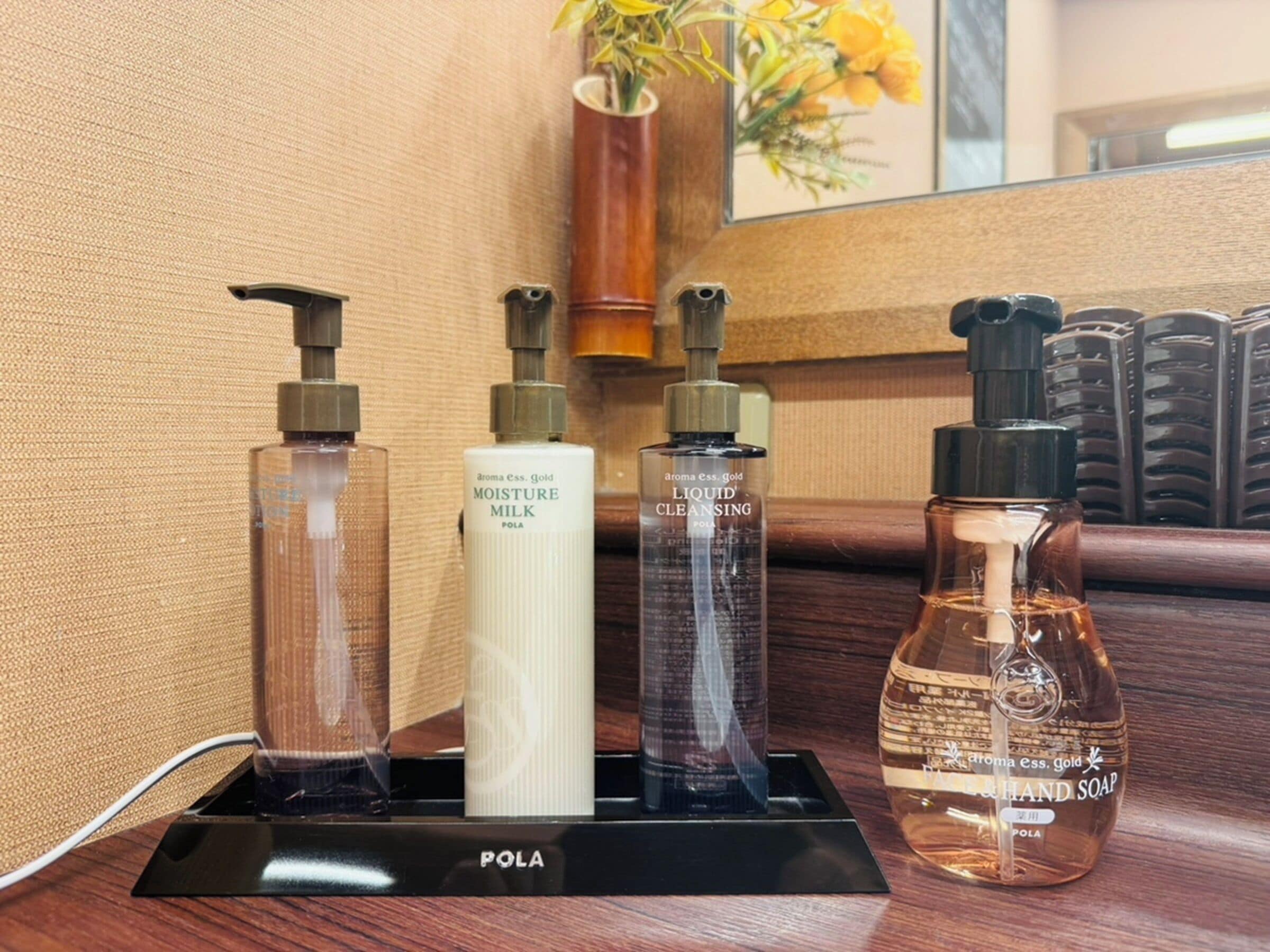 A set of toiletries including a bottle of liquid cleansing, a bottle of milk, and a bottle of hand soap, all placed on a black stand with the brand name 'POLA' visible.