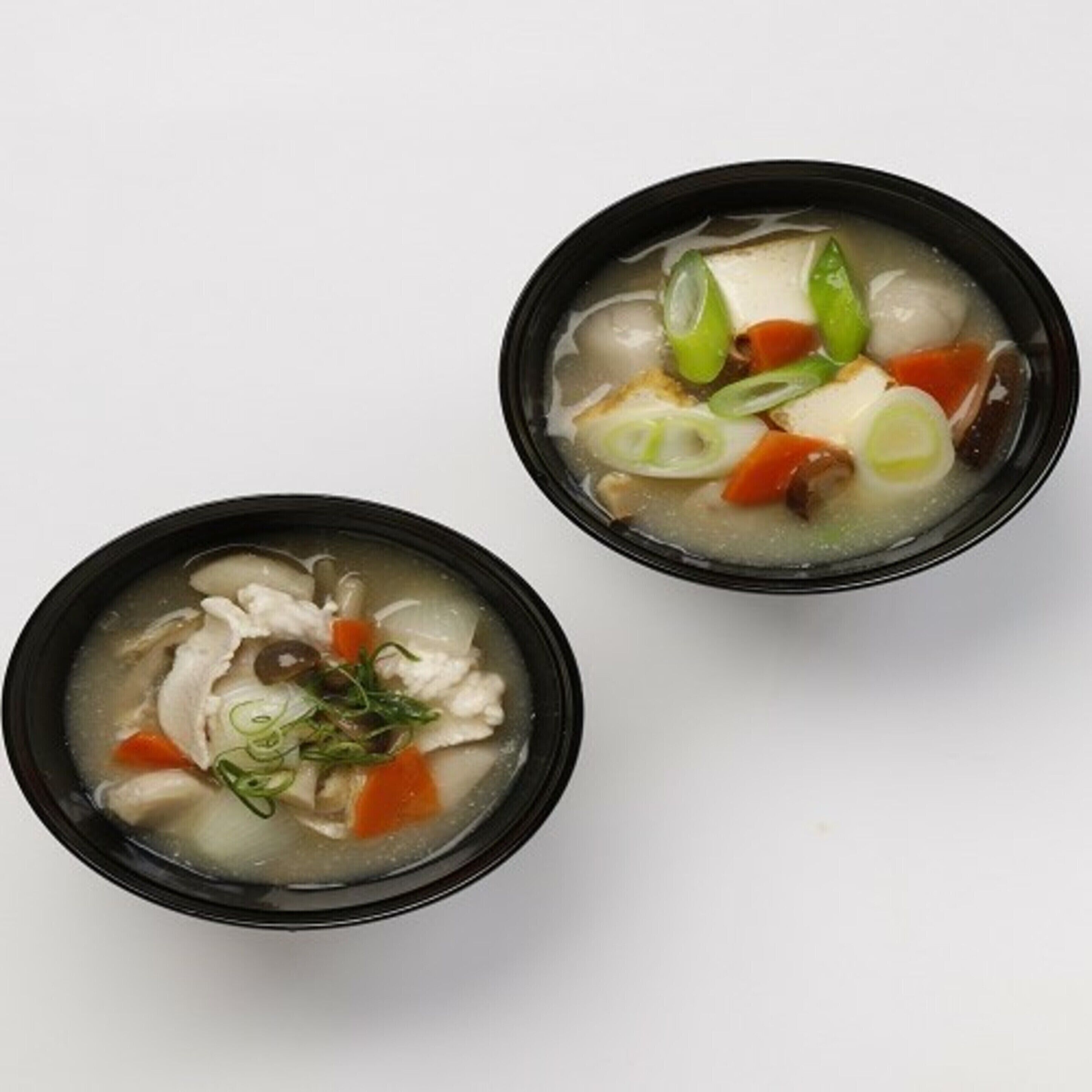 Two bowls of soup with various ingredients.