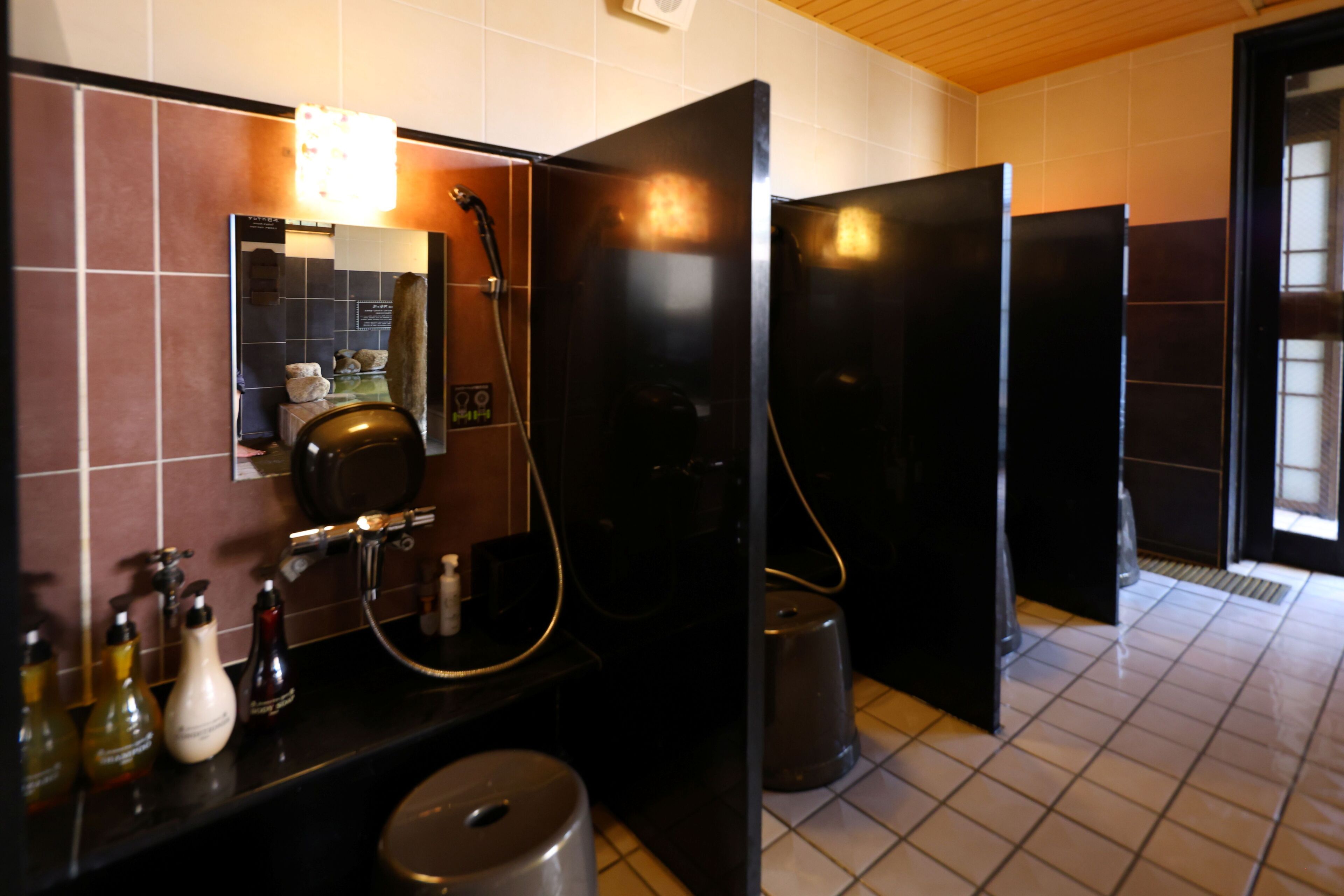 Un baño moderno con lavamanos negro, espejo y cabinas de inodoro negras.